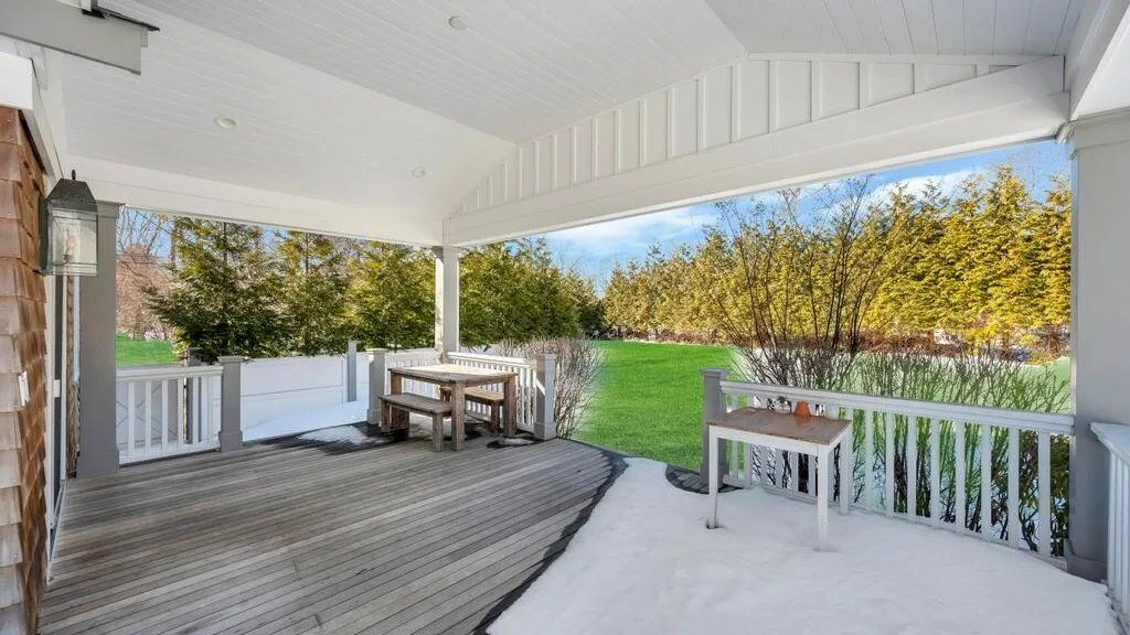 A covered outdoor deck with a dining table and seating overlooks a green lawn.
