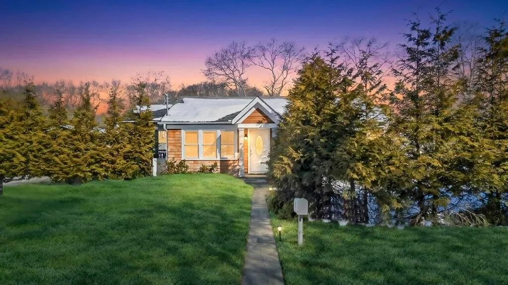 A house stands beside a grassy lawn and hedge beneath a colorful evening sky.