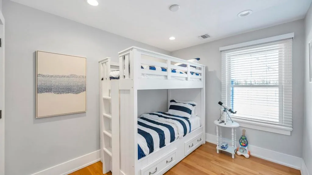 A bright bedroom features white bunk beds with blue-and-white striped bedding.