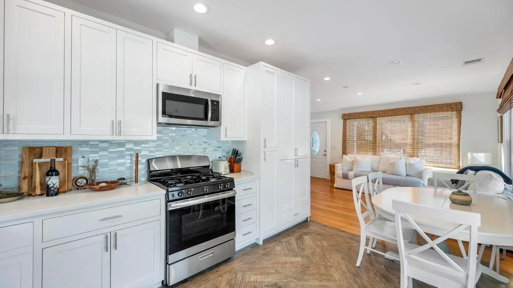 A bright open-plan kitchen and dining area with white cabinetry and a table.