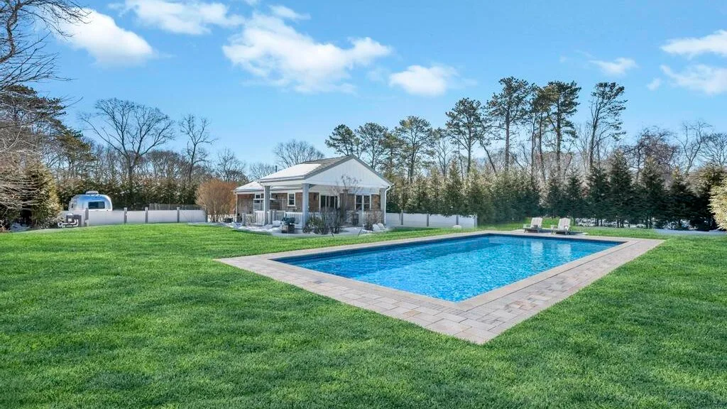 An outdoor swimming pool sits beside a grassy lawn and a small pavilion.