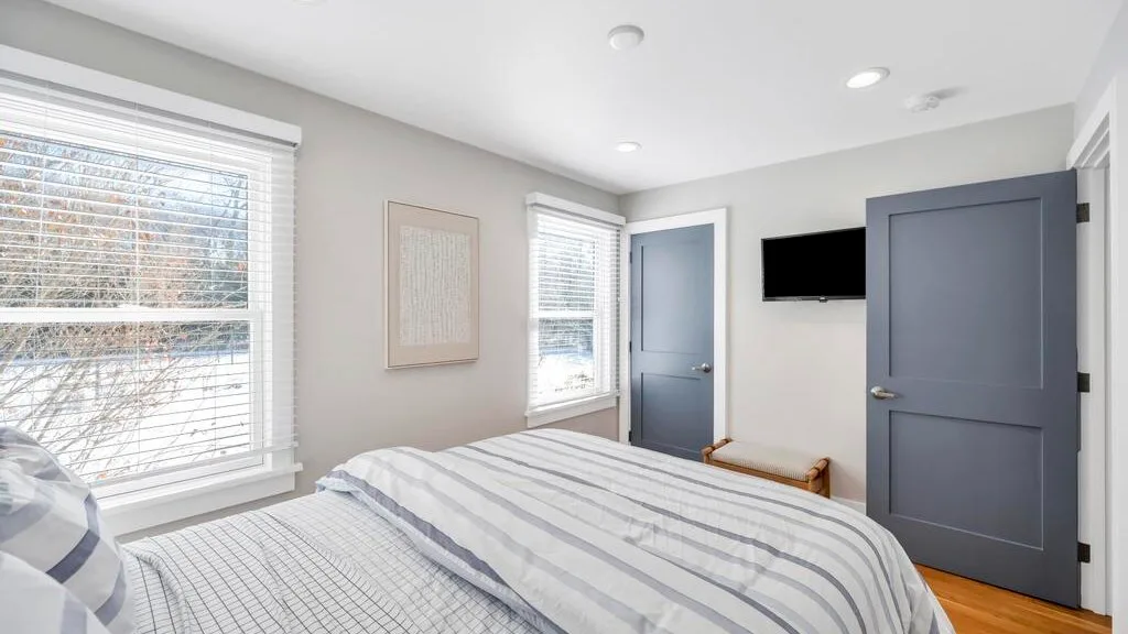 A bedroom with a bed, windows, and a wall-mounted television.