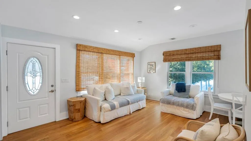 A bright living room with seating, a white entry door, and large windows.