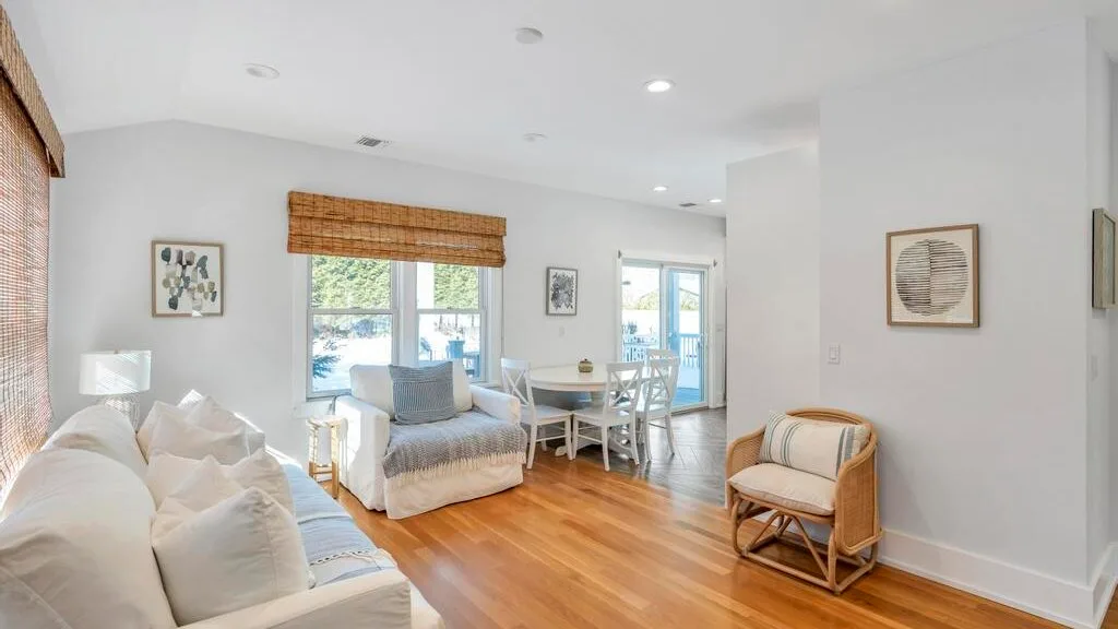 A bright living and dining area with seating beside a table and large windows.