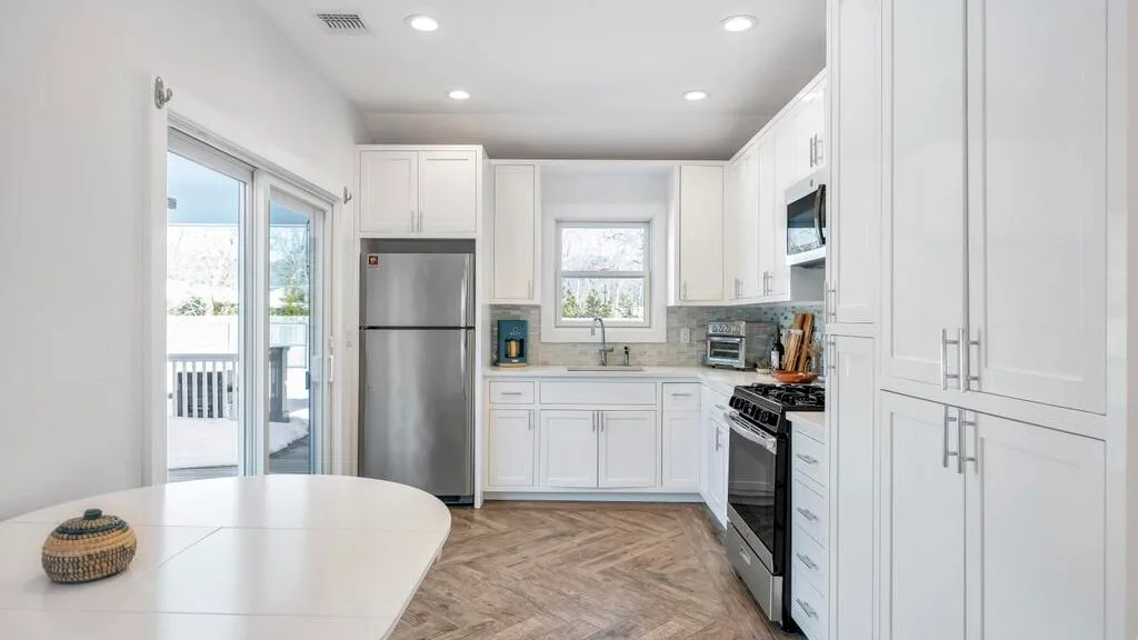 A bright kitchen with white cabinets, stainless steel appliances, and a dining table.