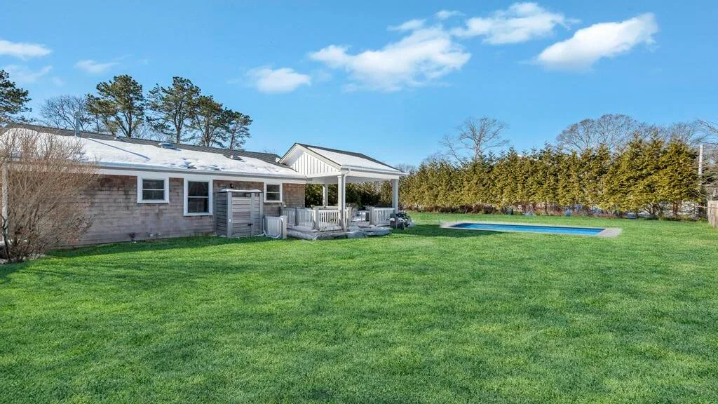 A single-story house and covered patio overlook a broad lawn and swimming pool.