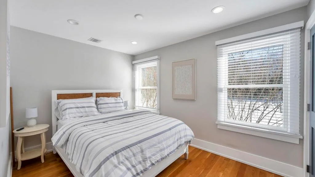 A bright bedroom with a neatly made bed and large windows.