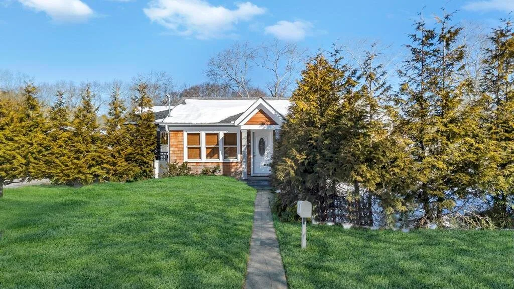 A small house stands beyond a green lawn, with a walkway leading to its entrance.