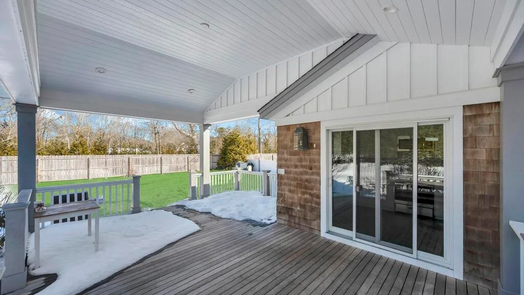 A covered wooden deck overlooks a lawn, with snow along the edges.