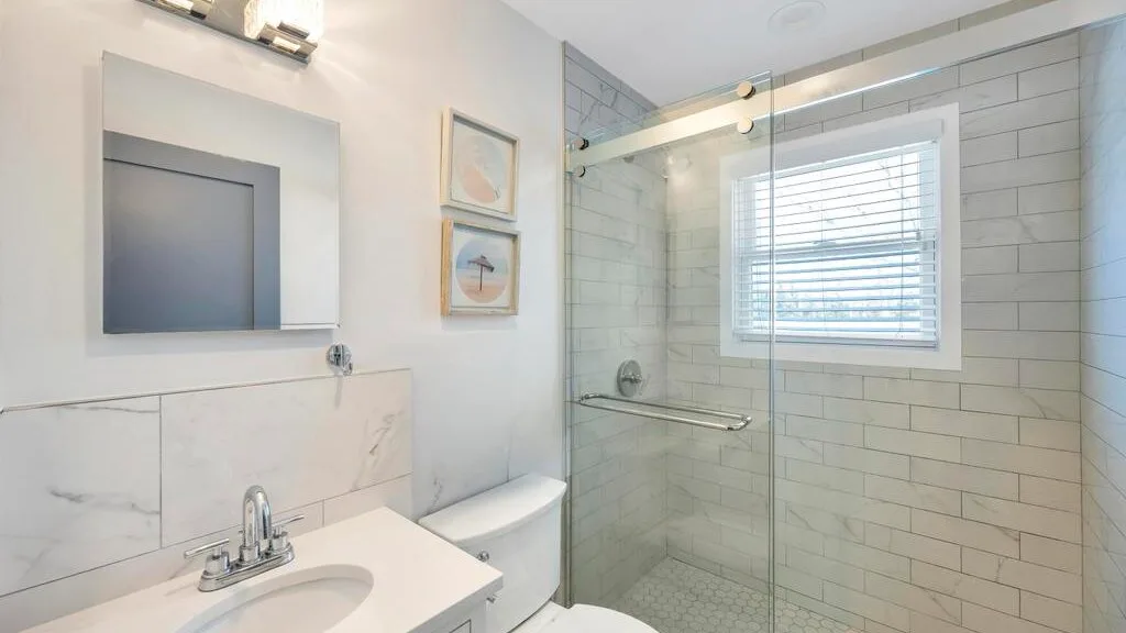 A bright bathroom with a glass shower and a window with blinds.