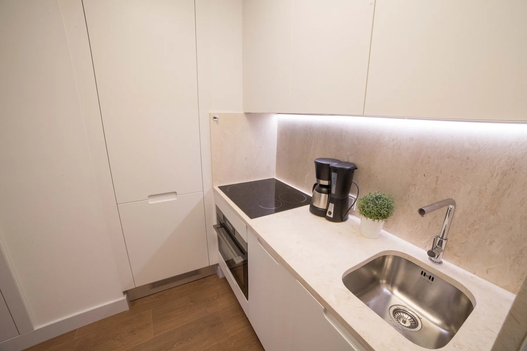 Una cocina compacta con placa de cocción, cafetera y fregadero.