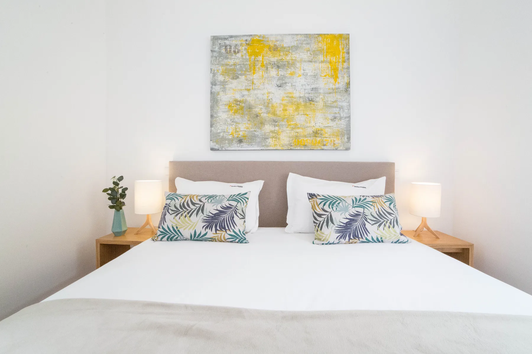 Dormitorio con una cama bien hecha y una obra colorida sobre el cabecero.