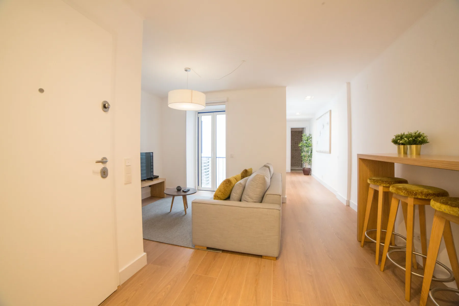 Una sala luminosa con asientos, un televisor y una pequeña barra de comedor.