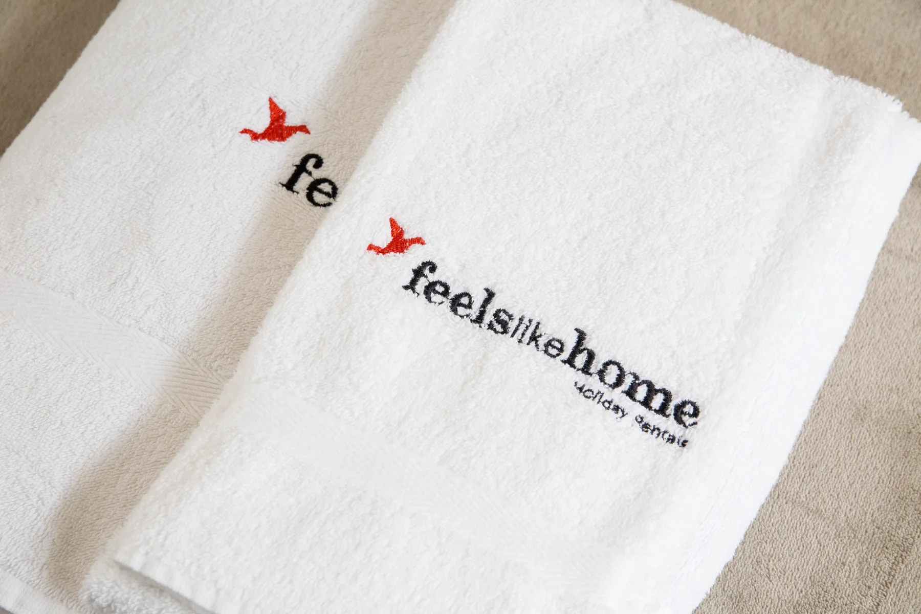 Toallas blancas con letras bordadas sobre una superficie beige.