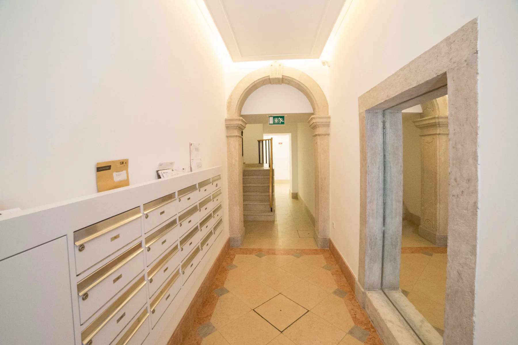 Pasillo de un edificio con filas de buzones y una puerta arqueada.
