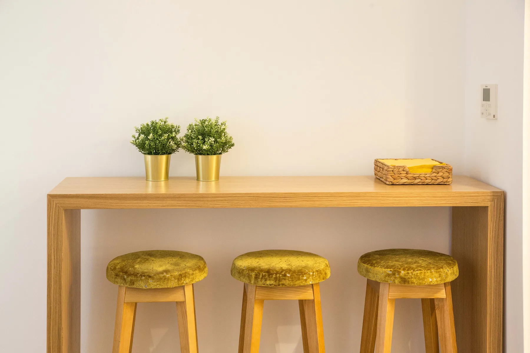Una barra de madera con taburetes y pequeñas plantas en macetas junto a una pared clara.