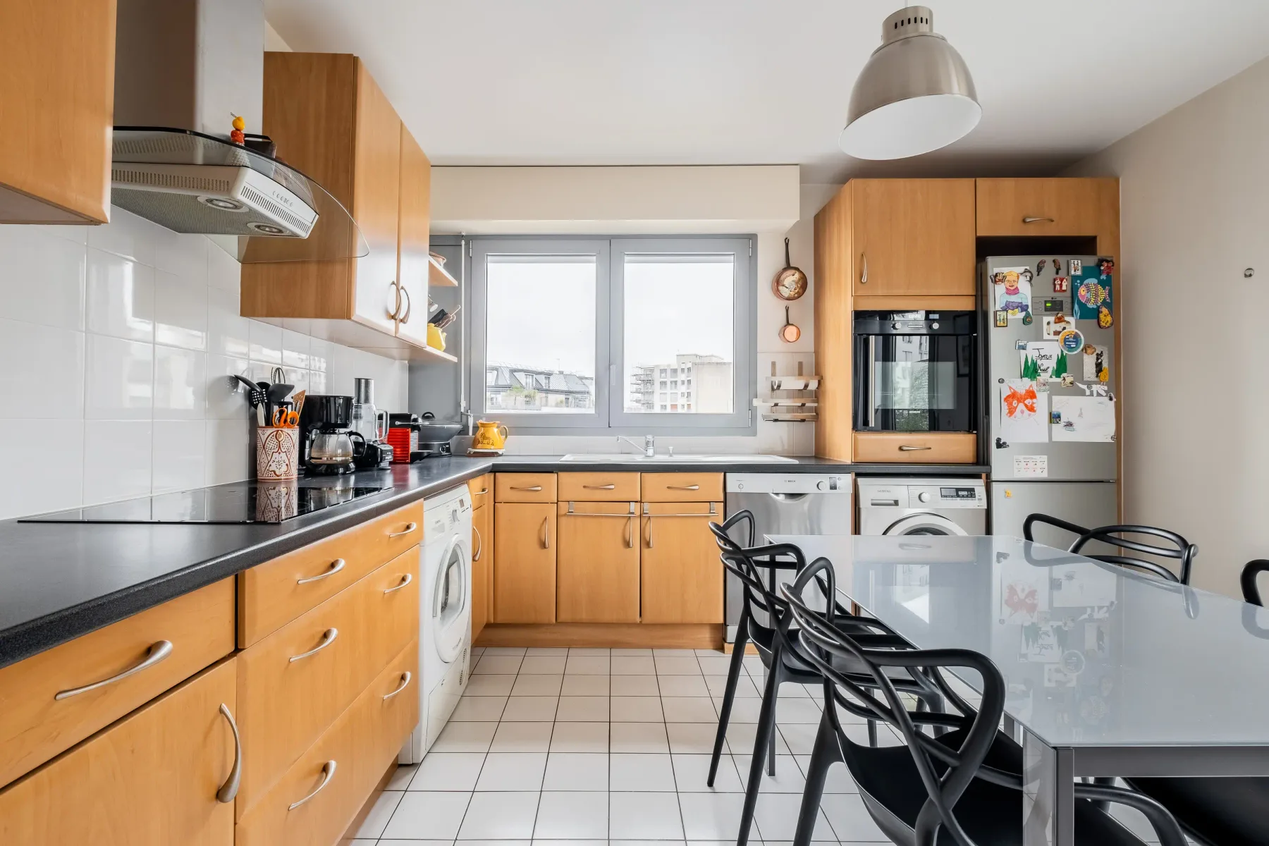 A bright kitchen with wooden cabinets, a central window, and a dining table.