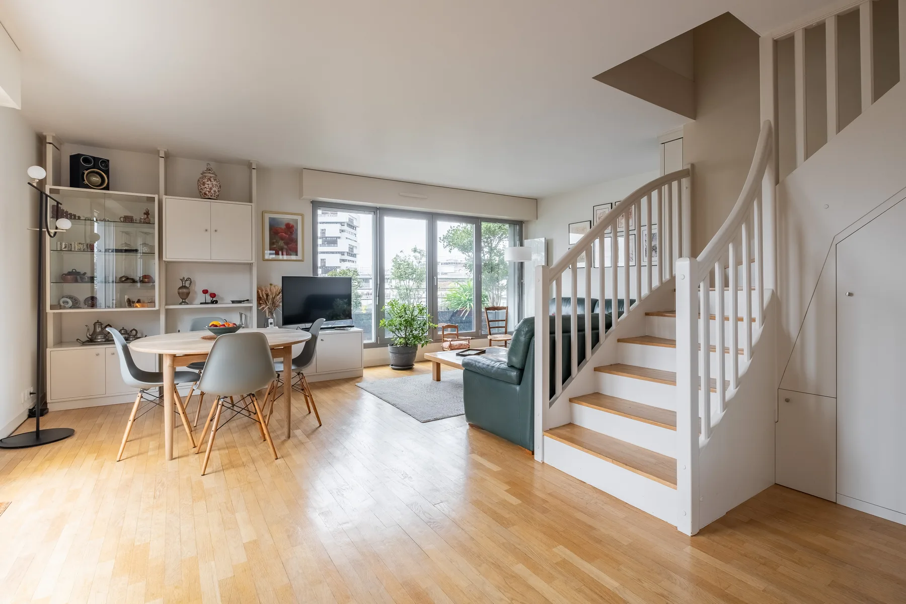 A bright living and dining area with large windows and a staircase.