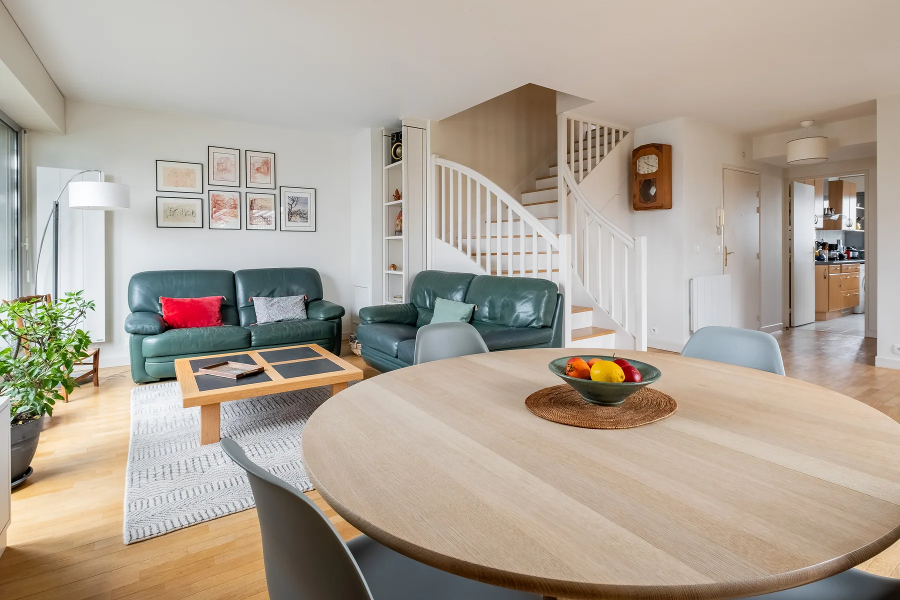A bright living room with green seating, a round dining table, and a staircase.