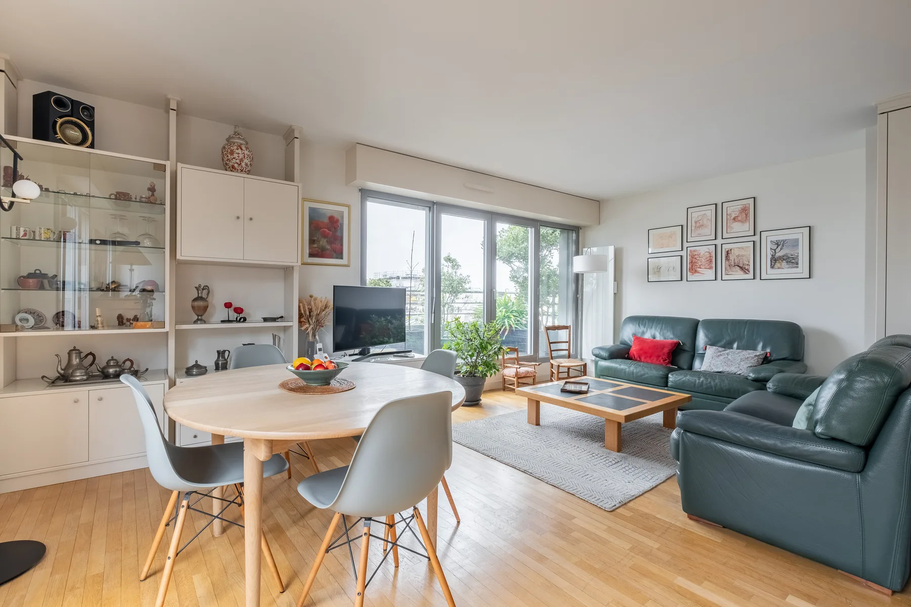 A bright living room has a dining table, television, and seating beside large windows.