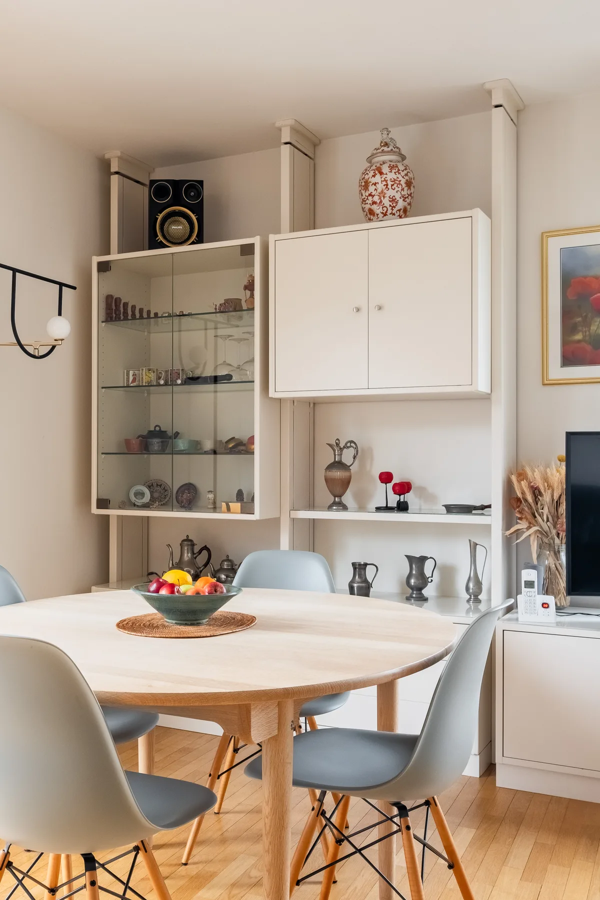 A dining area with a round table, seating, and display cabinets along the wall.