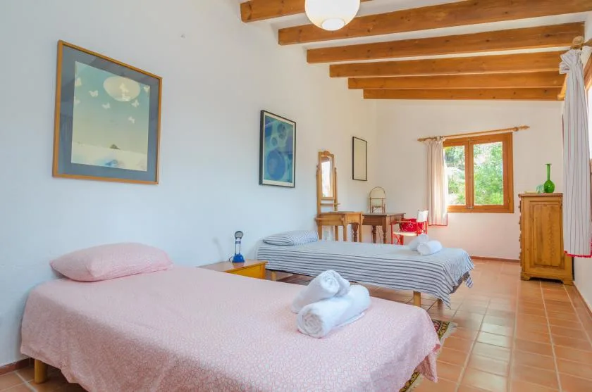 Un dormitorio luminoso con dos camas, vigas de madera y una ventana.