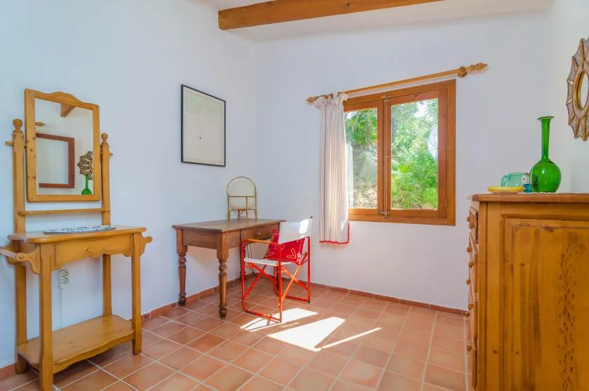 Una habitación luminosa con ventana de marco de madera, escritorio y silla roja.