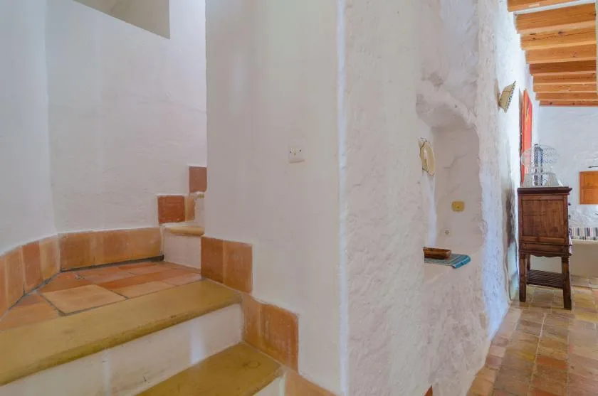 Una escalera de azulejos junto a una pared blanca de yeso conduce a una habitación con vigas de madera.