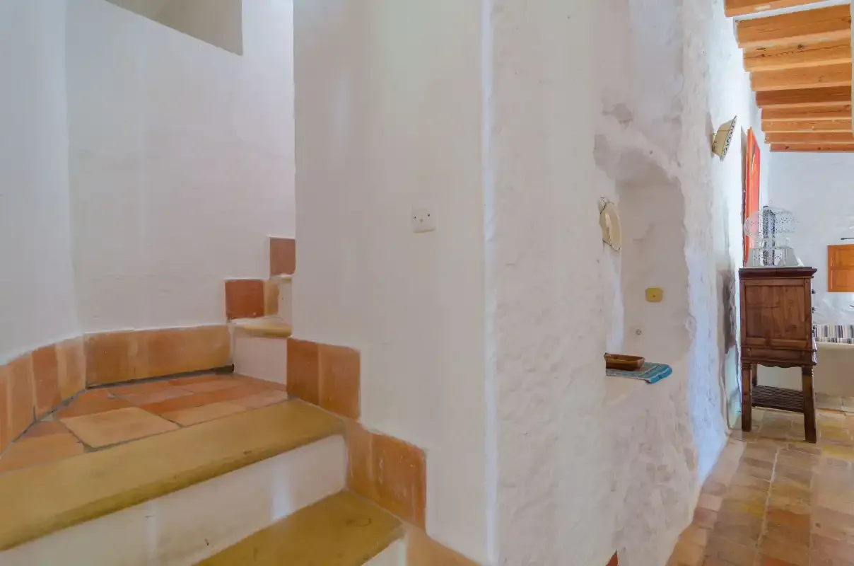 Un pasillo interior encalado con escalones de baldosas y vigas de madera vistas.