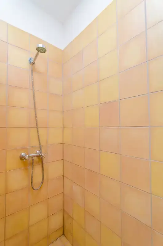 Una ducha alicatada con cabezal y controles montados en la pared.