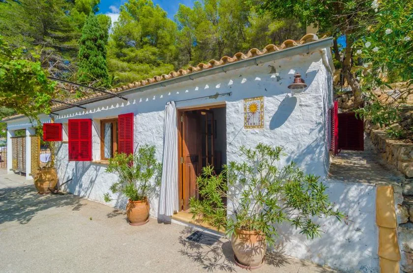 Una casa blanca con contraventanas rojas y una entrada abierta rodeada de plantas en macetas.