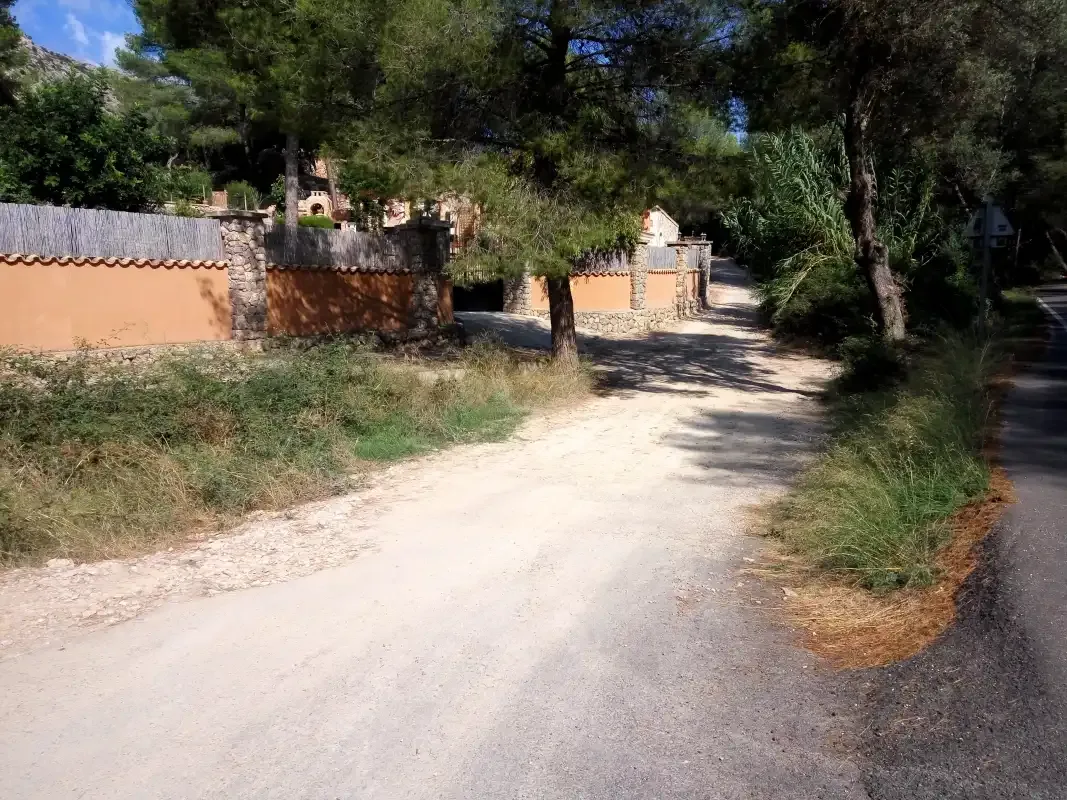 Un camino de tierra pasa junto a un muro bajo y árboles.