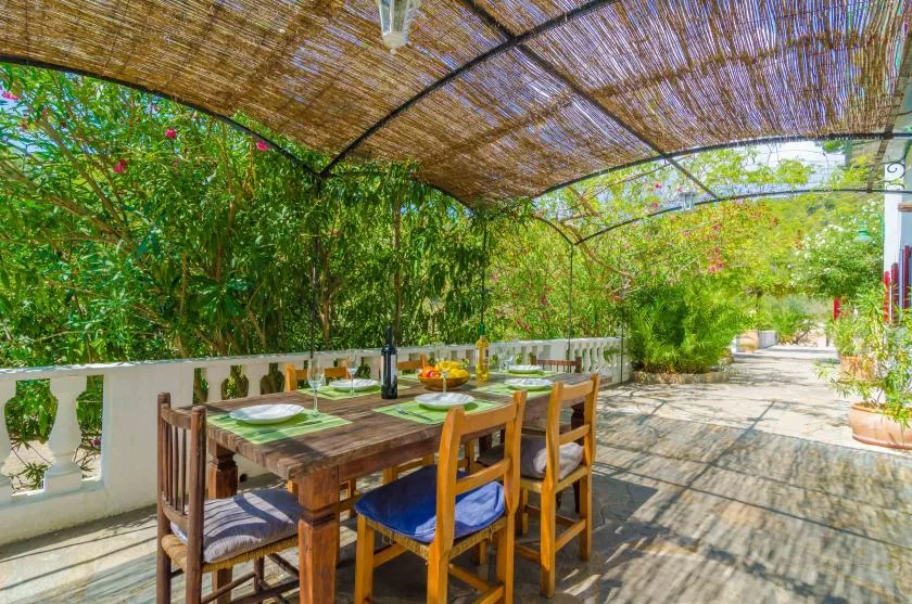 Un comedor al aire libre está bajo un toldo tejido, rodeado de vegetación.