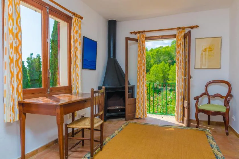 Un salón luminoso con una mesa de madera y puertas abiertas al balcón, frente a la vegetación.