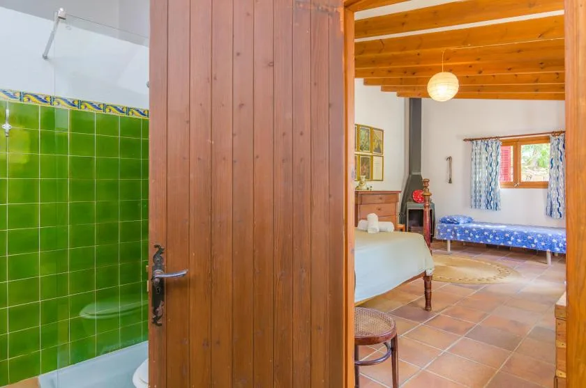 Un baño alicatado se abre a un dormitorio con vigas de madera y camas.