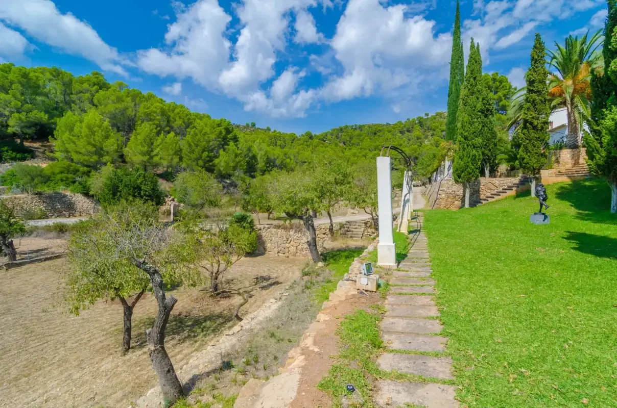 Un sendero de jardín transcurre entre un césped verde y una ladera seca con árboles.