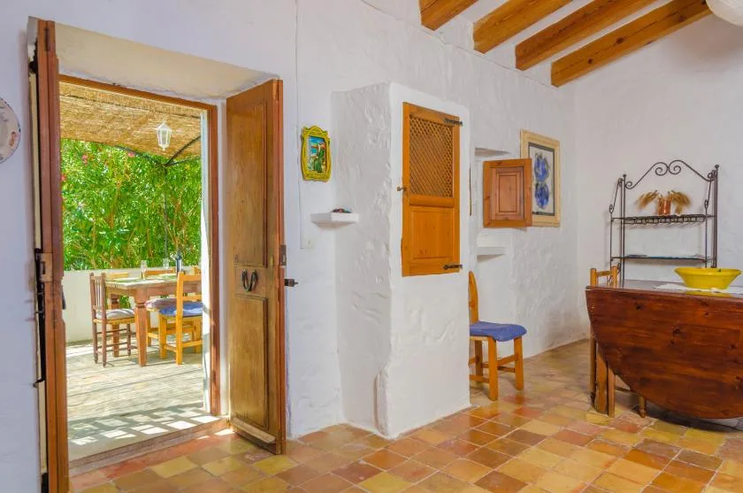Una estancia rústica con contraventanas de madera, suelo de baldosas y una puerta abierta al patio.