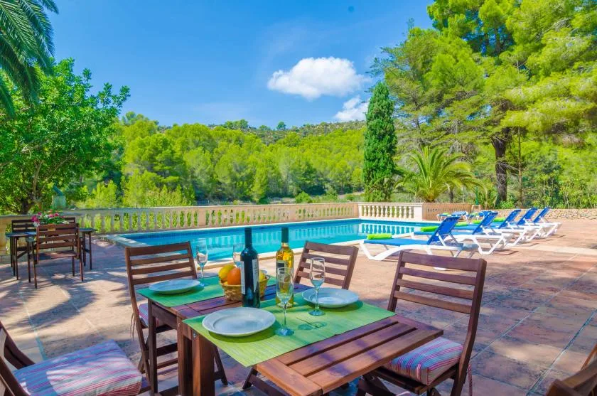 A poolside dining table overlooks a swimming pool and surrounding greenery.
