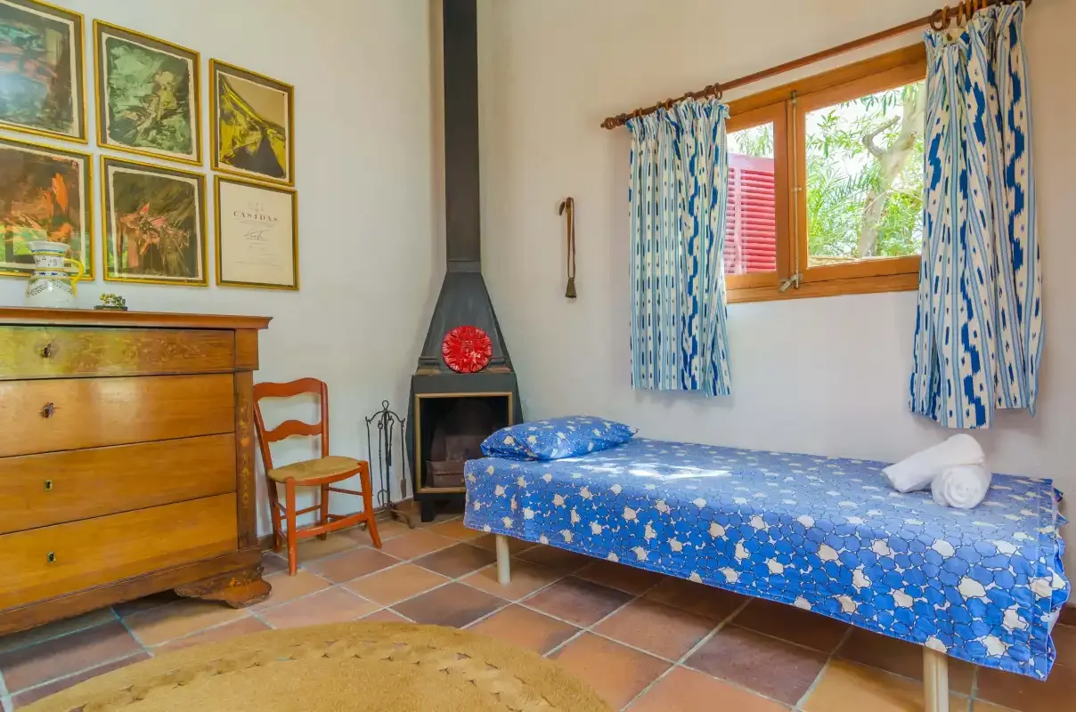 Un dormitorio con una colcha azul estampada y una ventana con cortinas.