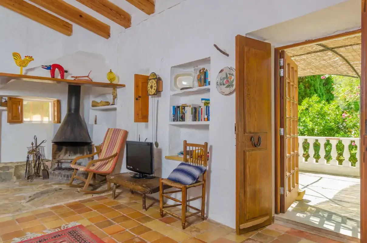 Un salón luminoso con chimenea y una puerta abierta a un balcón.
