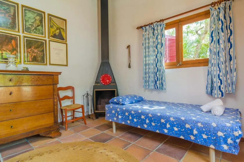 Un dormitorio con una cama individual, una cómoda de madera y una ventana con cortinas estampadas.