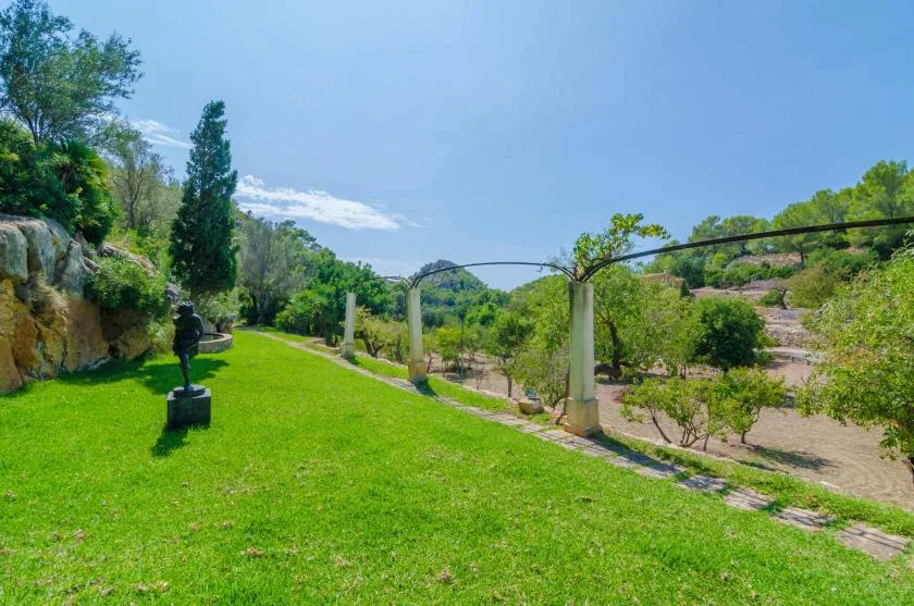Un jardín cuidado con césped verde, árboles y una pequeña escultura.
