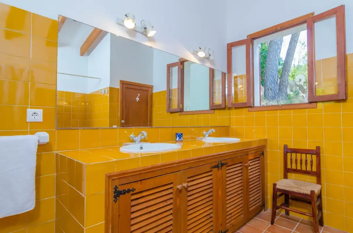 Un baño con una larga encimera de lavabos, armarios de madera y una ventana.