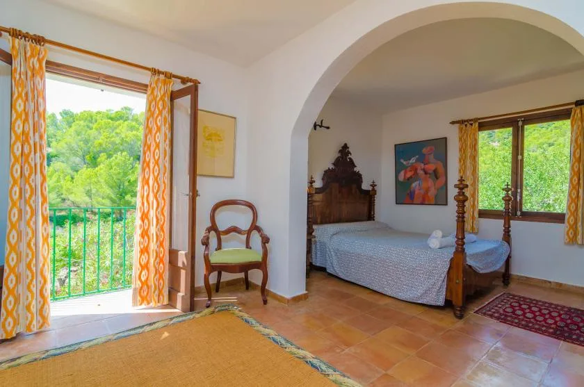 Un dormitorio con una cama de madera y ventanas con vista a árboles verdes.