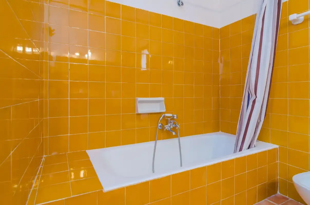 Una bañera está junto a paredes de azulejos naranjas en un baño.