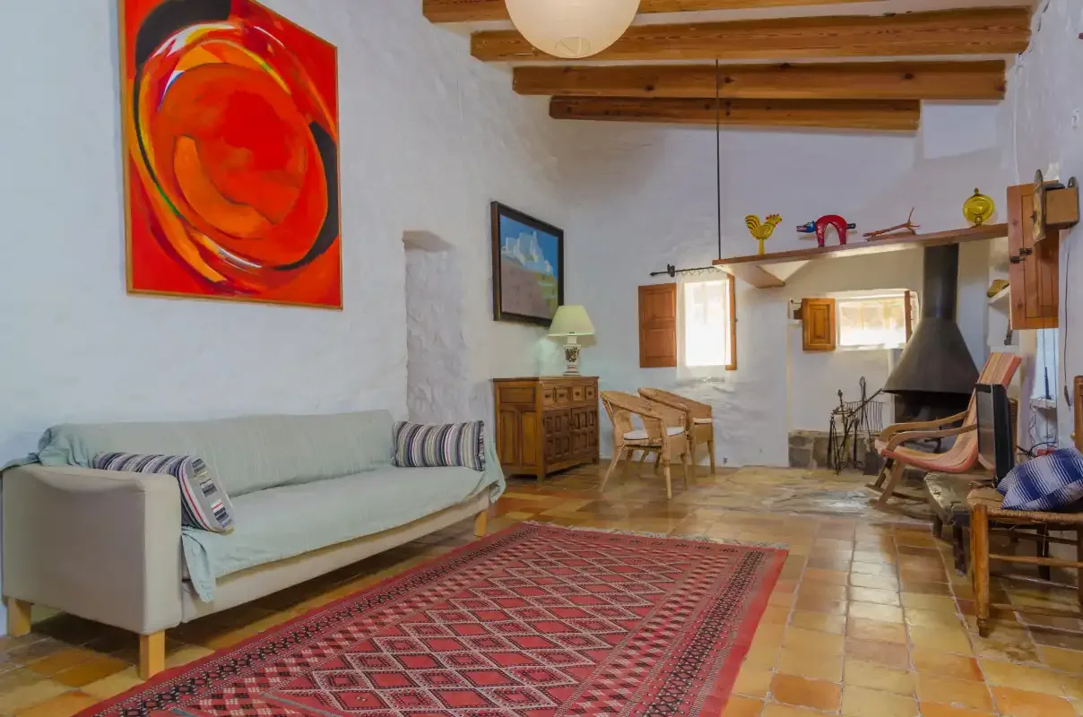 Una sala de estar con asientos, una alfombra estampada y vigas de madera a la vista.