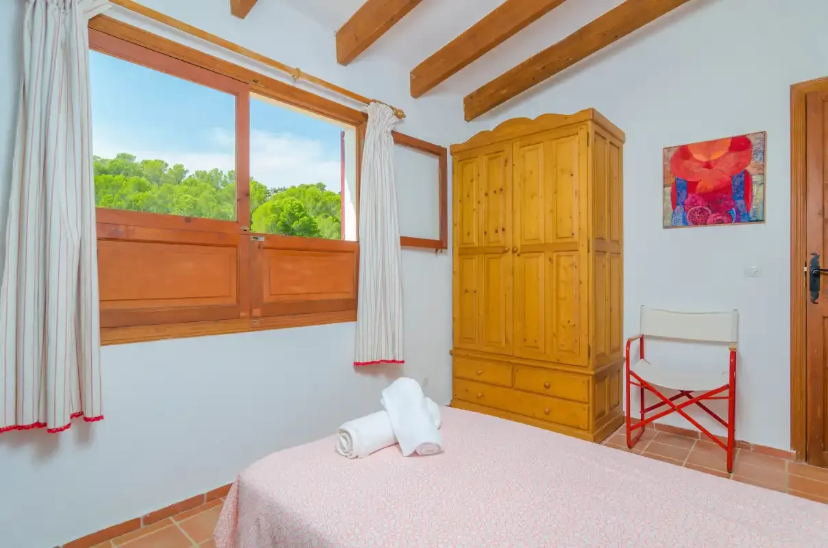 Un dormitorio con una cama junto a un armario de madera y una ventana amplia.