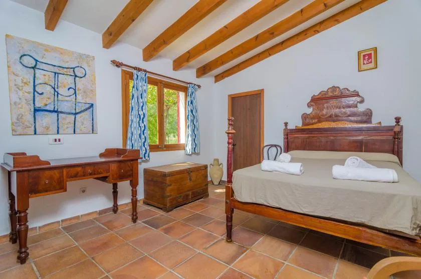 Dormitorio con una cama de madera, un escritorio y vigas de techo expuestas.