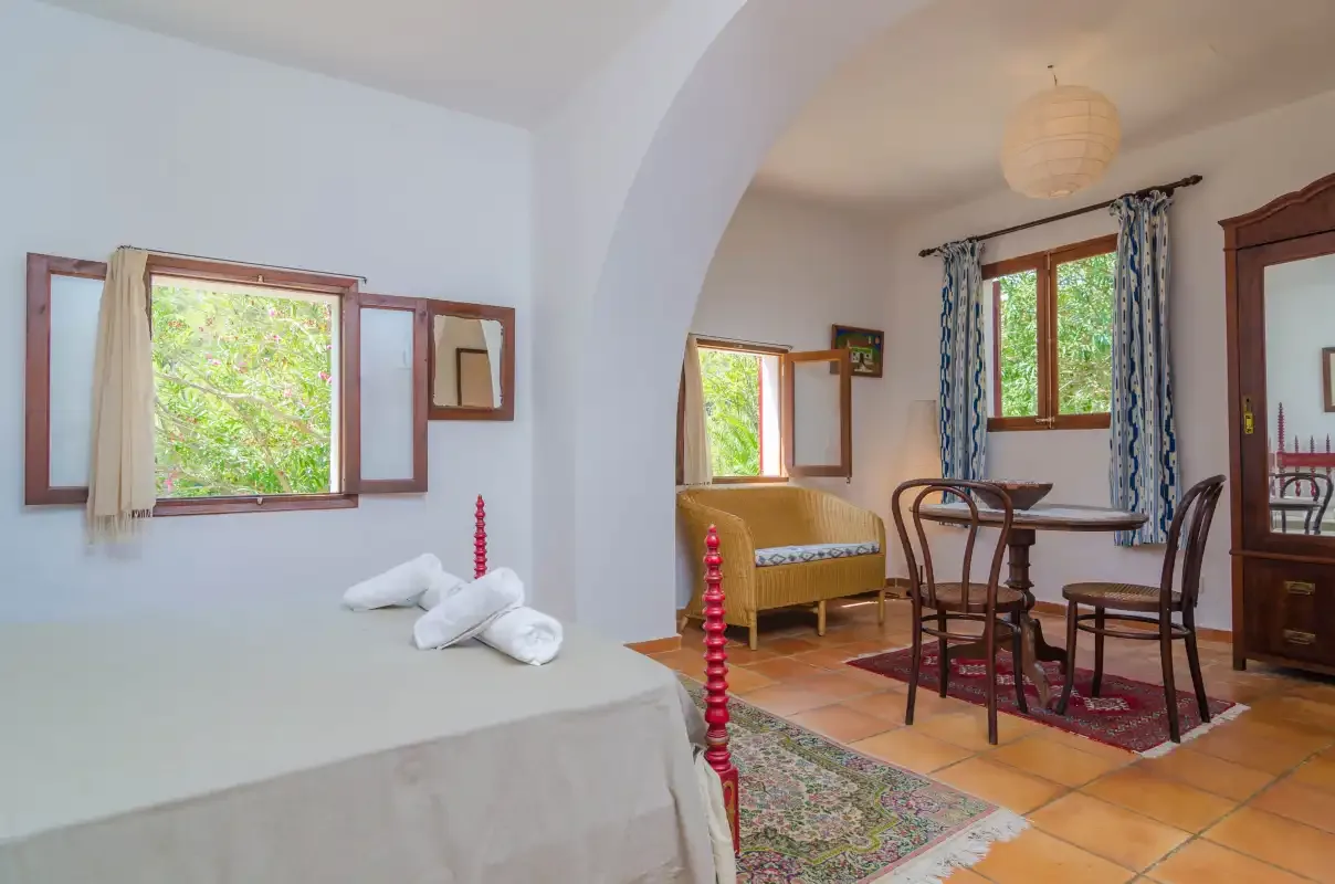 Un dormitorio y una zona de comedor comparten una estancia con arco, ventanas y suelo de baldosas.