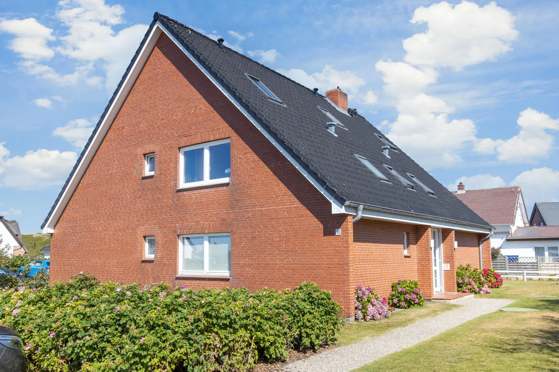 A red-brick house with a steep dark roof stands beside a garden path.